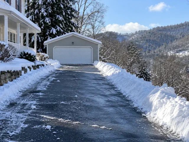 Plowed residential driveway to a detached garage with snow banked on the downhill side